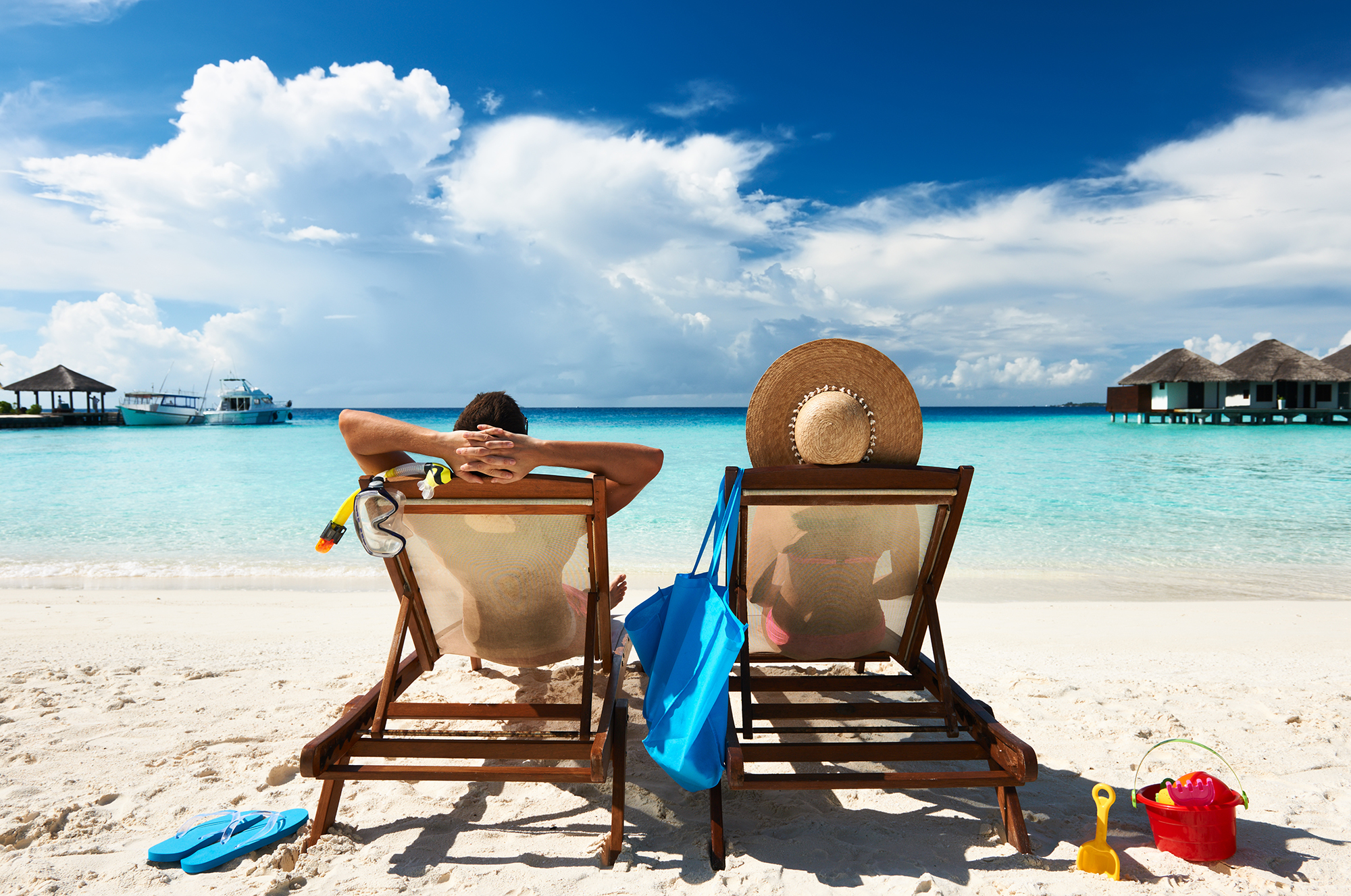 Two people relaxing on white sandy beach.