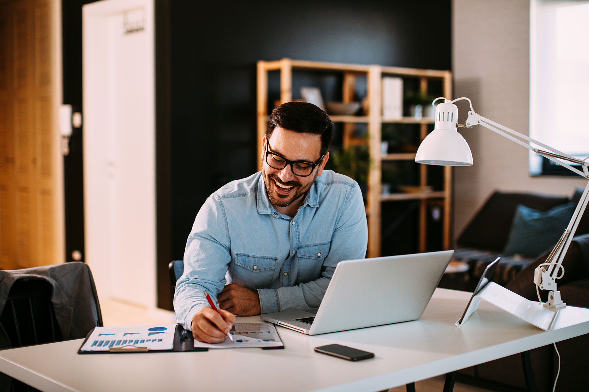 man smiling creating report at a desk with laptop