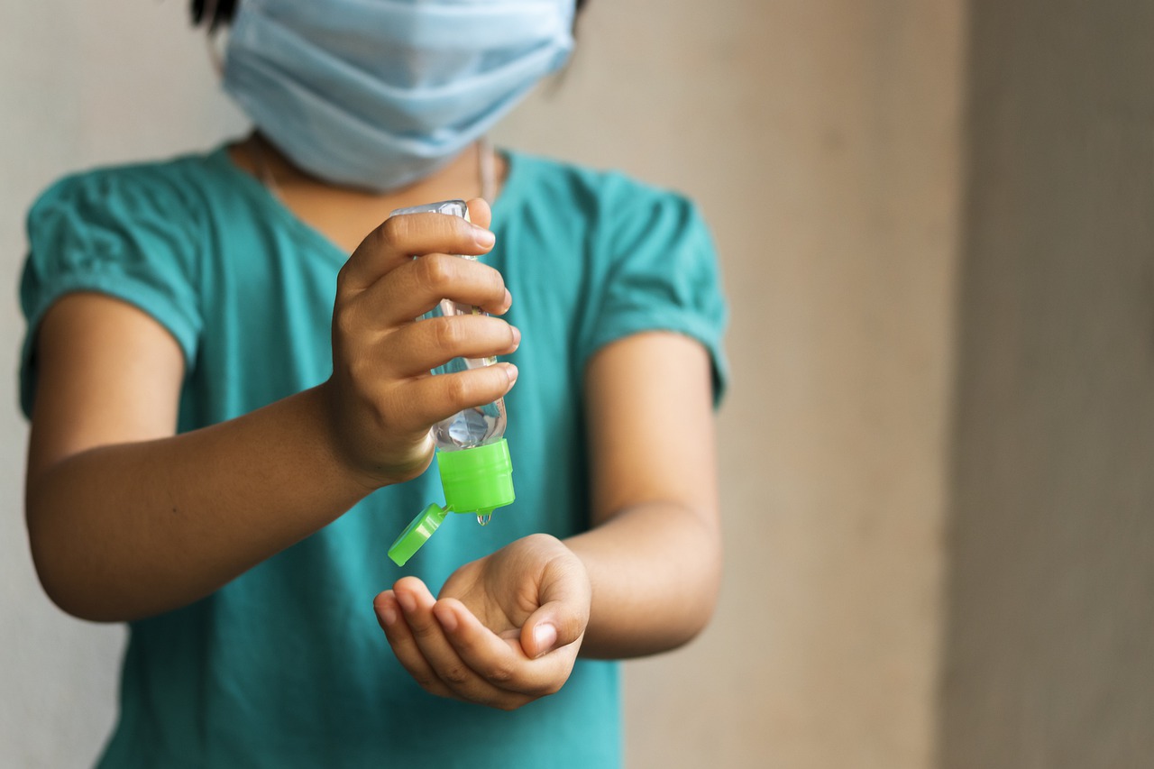 masked child putting on hand sanitizer