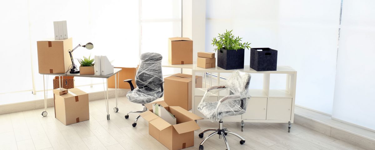 Office chairs and desks wrapped in plastic surrounded by boxes