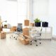 Office chairs and desks wrapped in plastic surrounded by boxes