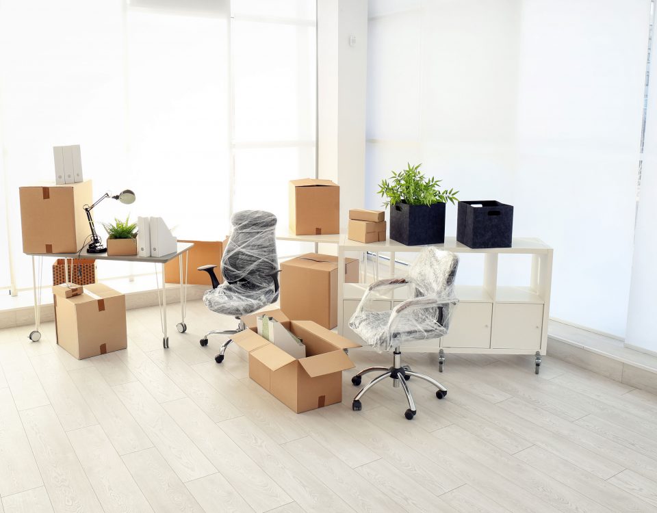 Office chairs and desks wrapped in plastic surrounded by boxes